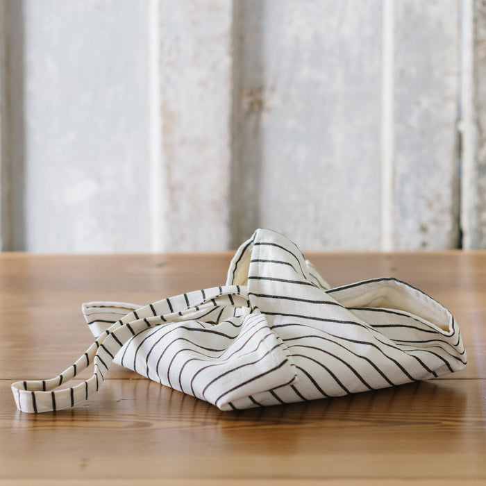 A folded striped picnic bag with a sling, laying on a wooden surface.