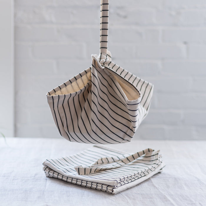 A striped picnic bag with a sling, hanging against a white background with another one folded on the table below.