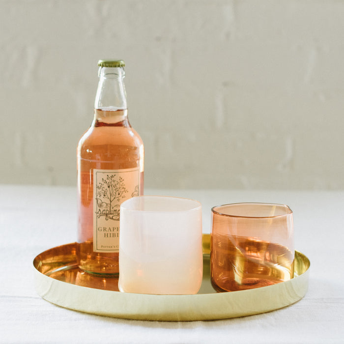 Two handcrafted, mouthblown glass cups and a bottle of grapefruit juice.