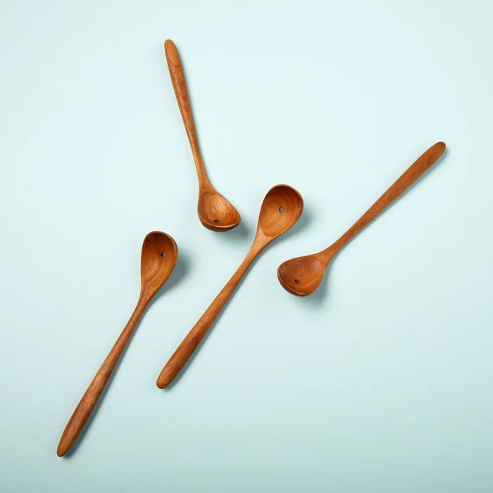 four spoons made from teak wood with a whole in the bottom of each spoon to drain liquids. The spoons sits on a blue background