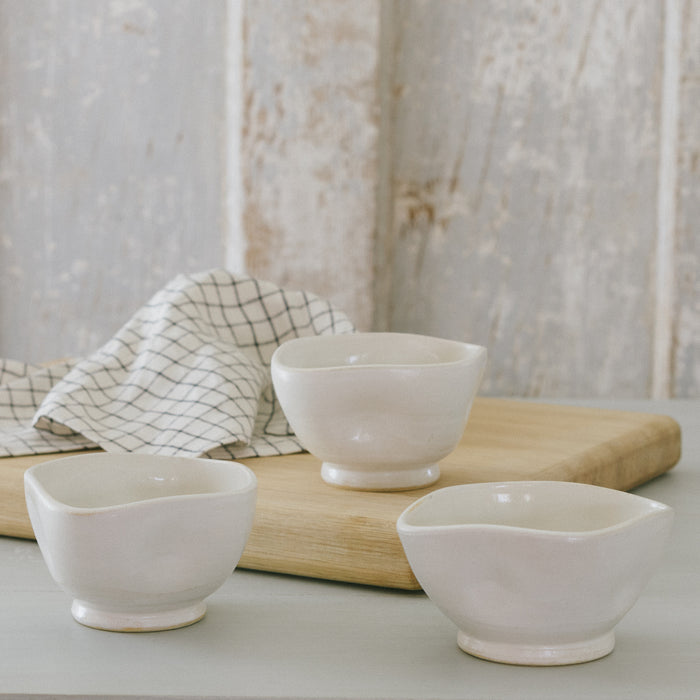 Three white stoneware bowls with white glaze on a wooden surface, with a checkered napkin in the background.